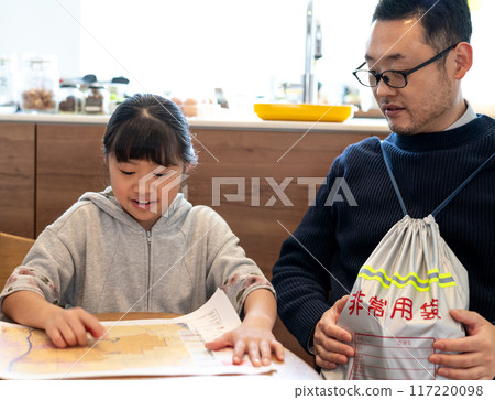 A daughter checking the location of her house on a hazard map while her father looks on, carrying an emergency kit A daughter checking the location of her house on a hazard map while her father looks on, carrying an emergency kit 117220098