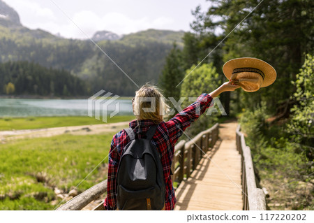 Woman traveler wearing hat and looking at amazing mountains and lake, wanderlust travel concept. black lake Montenegro. 117220202
