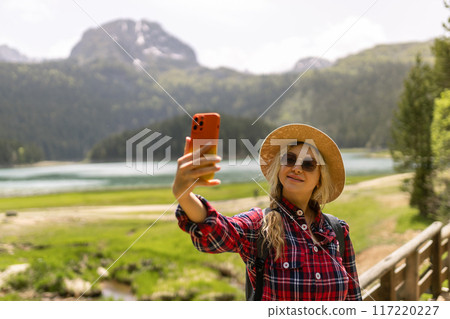 Selfie while traveling. Landscape with young woman, green hills and lake. Lifestyle, adventure, nature, active life. Selfie while traveling. Landscape with young woman, green hills and lake. Lifestyle, adventure, nature, active life. 117220227