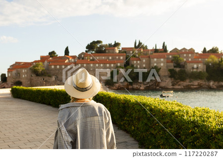 girl tourist in a hat looks from a top on the island of Sveti Stefan in Montenegro and the sea 117220287