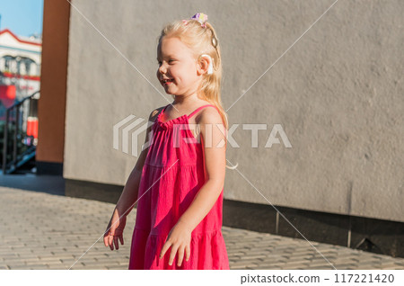 Funny baby with cochlear implant walks outdoor copy space. Hearing aid and medicine innovating technology concept. Diversity and Inclusion and people with disability concept. 117221420