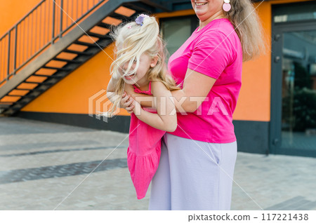 Deaf child with cochlear implant for hearing audio and aid for impairment having fun and laughs with mother outdoor in summer. Sound fitting device to help with communication listening and interaction 117221438