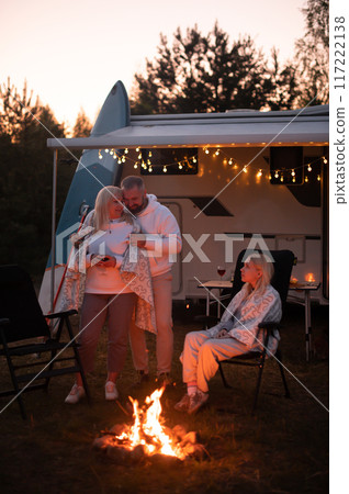 The family is relaxing together by the campfire near their mobile home. Evening family vacation The family is relaxing together by the campfire near their mobile home. Evening family vacation 117222138