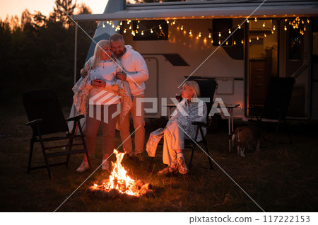 The family is relaxing together by the campfire near their mobile home. Evening family vacation The family is relaxing together by the campfire near their mobile home. Evening family vacation 117222153