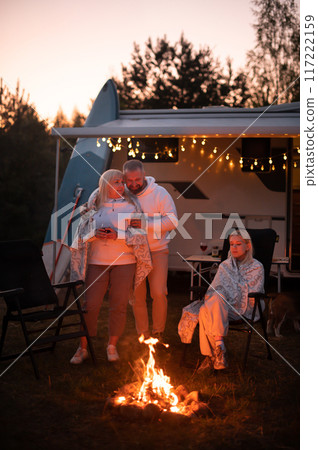 The family is relaxing together by the campfire near their mobile home. Evening family vacation The family is relaxing together by the campfire near their mobile home. Evening family vacation 117222159