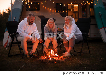 A family cooks sausages on a bonfire near their motorhome in the woods A family cooks sausages on a bonfire near their motorhome in the woods 117222191