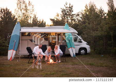 A family cooks sausages on a bonfire near their motorhome in the woods A family cooks sausages on a bonfire near their motorhome in the woods 117222197