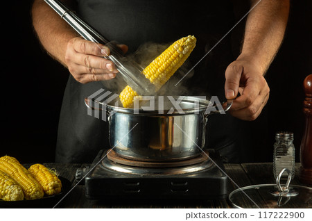 A cook prepares corn for dinner at a tavern. A head of hot corn with steam in tongs to check for doneness. Corn menu A cook prepares corn for dinner at a tavern. A head of hot corn with steam in tongs to check for doneness. Corn menu 117222900