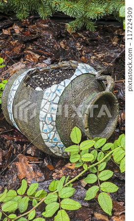 Decorative jug in the garden near flowers and trees. Rainy weather. 117224309