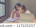 Two young women working with laptop and paperwork in discussion 117225257
