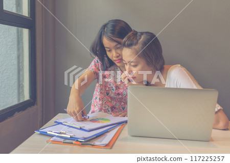 Two young women working with laptop and paperwork in discussion 117225257