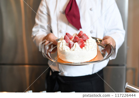 Hand holding a whole cake with short cream and strawberries 117226444