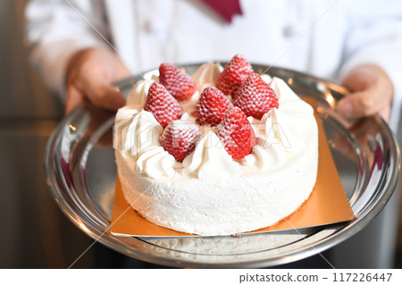 Hand holding a whole cake with short cream and strawberries 117226447