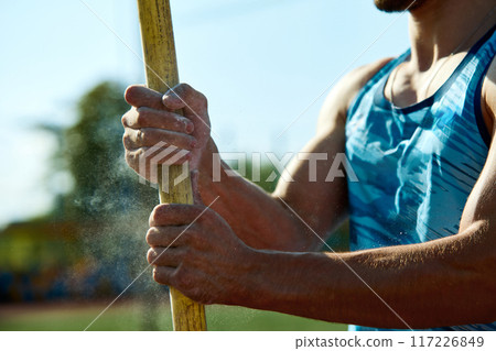 Cropped image of male athlete holding pole with hands in chalk. Determined young man preparing for pole jump, showcasing strength and readiness Cropped image of male athlete holding pole with hands in chalk. Determined young man preparing for pole jump, showcasing strength and readiness 117226849