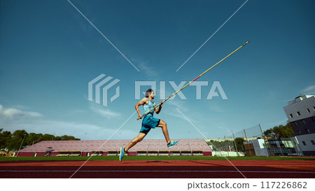 High jump training in progress, with a strong and focused pole vaulter in motion, running wit pole at outdoor stadium High jump training in progress, with a strong and focused pole vaulter in motion, running wit pole at outdoor stadium 117226862