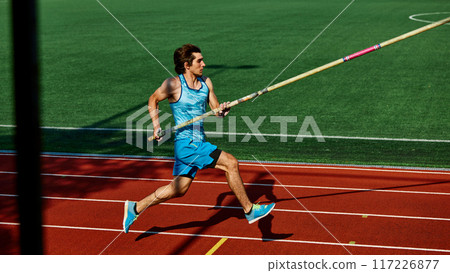 High jump practice session, with focused and strong young man, pole vaulter in blue uniform in motion, running with pole at outdoor stadium High jump practice session, with focused and strong young man, pole vaulter in blue uniform in motion, running with pole at outdoor stadium 117226877