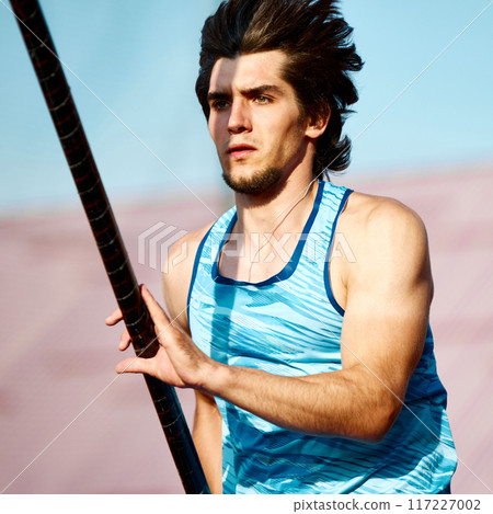 Portrait of focused young man, pole vaulting athlete in blue uniform in motion with pole, preparing for high jump at outdoor stadium 117227002