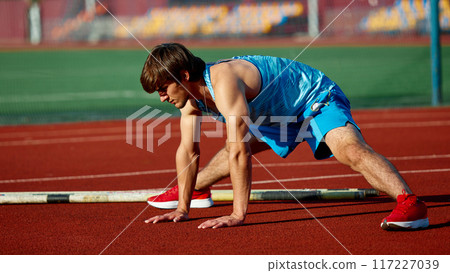 Intensive training under sun. Muscular athlete, young man in uniform, pole vaulter preparing for enduring training session at open air stadium. Intensive training under sun. Muscular athlete, young man in uniform, pole vaulter preparing for enduring training session at open air stadium. 117227039