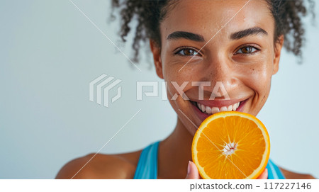 Joyful Nutrition: Close Portrait of a Happy Female Athlete and a Luscious Orange 117227146