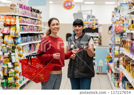 The sales consultant offers the buyer a new product in the supermarket. Two happy young Caucasian women. Concept of shopping, business and trade The sales consultant offers the buyer a new product in the supermarket. Two happy young Caucasian women. Concept of shopping, business and trade 117227654