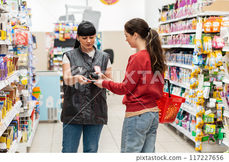 A supermarket sales consultant checks the expiration date of the product selected by the customer. Young women of Caucasian nationality. The concept of shopping and business A supermarket sales consultant checks the expiration date of the product selected by the customer. Young women of Caucasian nationality. The concept of shopping and business 117227656