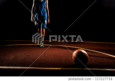 Basketball. A teenage boy in a blue sports uniform walks confidently towards a basketball ball lying on the Playground. Black background. Concept of sports games Basketball. A teenage boy in a blue sports uniform walks confidently towards a basketball ball lying on the Playground. Black background. Concept of sports games 117227718