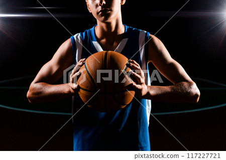 Basketball. Close up portrait of a teenage boy in blue sportswear confidently holds a basketball with muscular hands. Black background. Concept of sports games Basketball. Close up portrait of a teenage boy in blue sportswear confidently holds a basketball with muscular hands. Black background. Concept of sports games 117227721