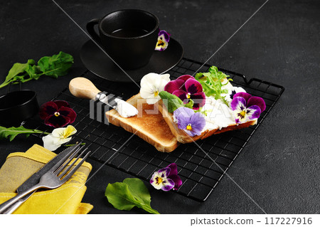 brioche toast with cream cheese and pansy flowers on a plate. Selective focus, black background, copy space brioche toast with cream cheese and pansy flowers on a plate. Selective focus, black background, copy space 117227916