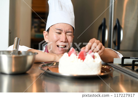 A male pastry chef struggling while arranging a cake 117227917
