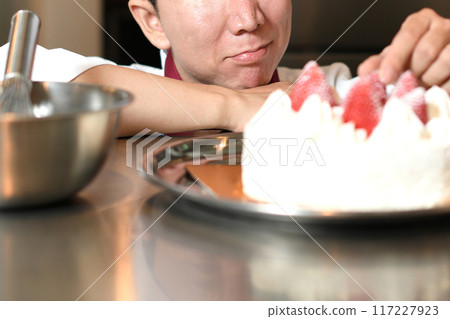 A male pastry chef struggling while arranging a cake 117227923