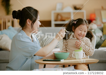 Asian mom smiling widely while feeding her little daughter in nursery 117228032