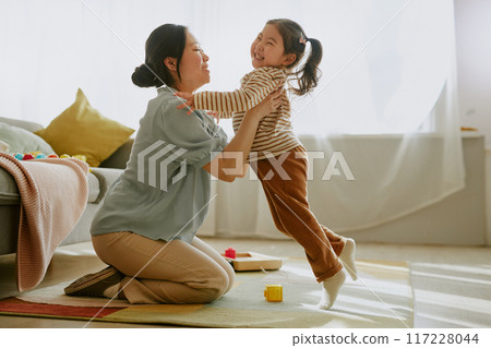 Asian mom sitting on floor and hugging her curious little girl in nursery 117228044