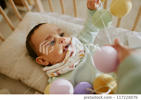 Unrecognizable female hand holding multicolored round rattle while his son enjoying playing Unrecognizable female hand holding multicolored round rattle while his son enjoying playing 117228076