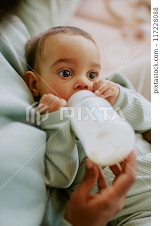 High angle shot of baby boy eating formula while his mother holding bottle and helping him to eat 117228088