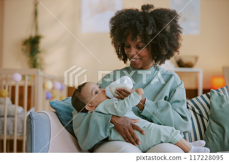 African American mother holding her son and feeding him while he looking around nursery and eating African American mother holding her son and feeding him while he looking around nursery and eating 117228095