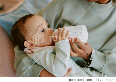 Medium close up of caring female hands holding her son and bottle with formula to feed baby 117228098