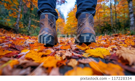 Legs in boots walking on path covered in bright autumn leaves. Fall season, forest. Low angle image 117228334
