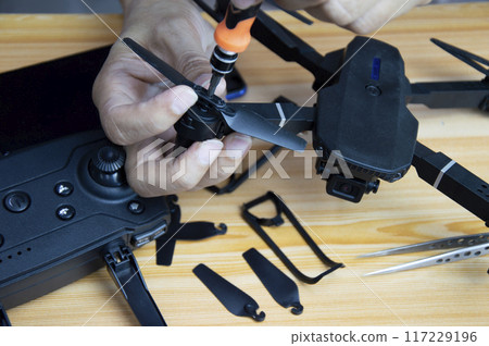 Professional mechanic repairing a drone with a small screwdriver on the table with various tools in modern workshop Professional mechanic repairing a drone with a small screwdriver on the table with various tools in modern workshop 117229196