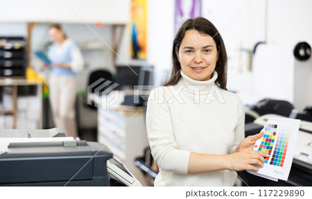 Portrait of positive woman printing office worker with colour test page Portrait of positive woman printing office worker with colour test page 117229890