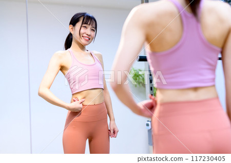 A young smiling woman who worries about her stomach at the sports gym Diet Personal gym Muscle training girl A young smiling woman who worries about her stomach at the sports gym Diet Personal gym Muscle training girl 117230405