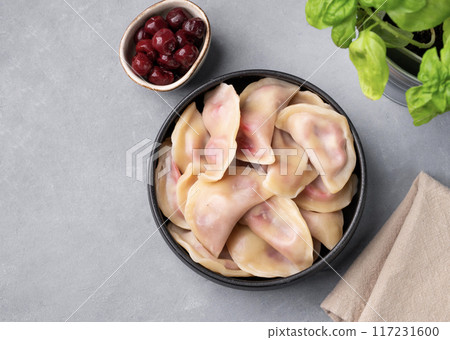 Dumplings with cherry. Delicious vegetarian vareniki with berries in a bowl on a gray background Dumplings with cherry. Delicious vegetarian vareniki with berries in a bowl on a gray background 117231600