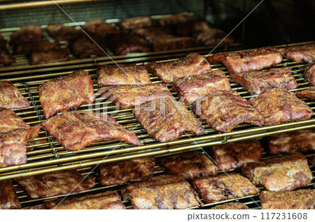 Grilled barbecue pork ribs in a smoker at the factory. The concept of a delicious snack Grilled barbecue pork ribs in a smoker at the factory. The concept of a delicious snack 117231608
