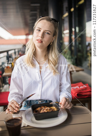 Blonde gen z woman eating lasagna in the cafe on break. Gen z girl spend time in restaurant 117231627