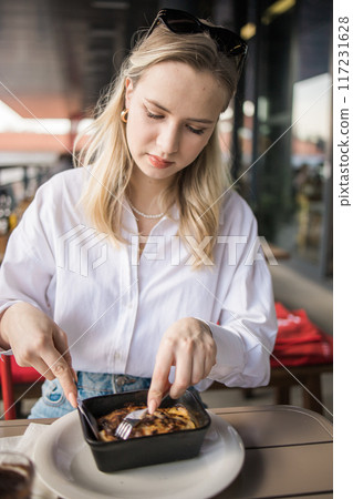 Blonde gen z woman eating lasagna in the cafe on break. Gen z girl spend time in restaurant 117231628
