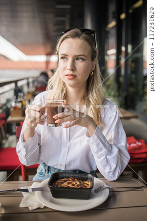 Blonde gen z woman eating lasagna in the cafe on break. Gen z girl spend time in restaurant 117231629