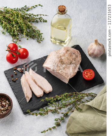 Baked chicken breast cut into pieces on a black slate board on a light background with fresh tomato 117231653