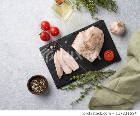 Baked chicken breast cut into pieces on a black slate board on a light background with fresh tomato Baked chicken breast cut into pieces on a black slate board on a light background with fresh tomato 117231654