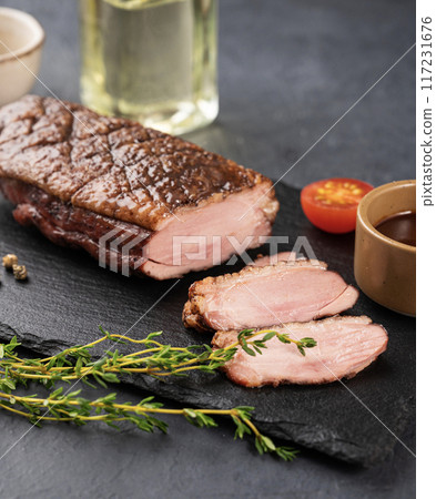 Grilled BBQ duck breast in marinade and spices with sauce on a slate board with fresh herbs Grilled BBQ duck breast in marinade and spices with sauce on a slate board with fresh herbs 117231676