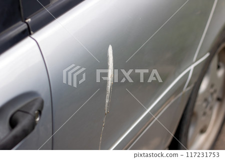 A silver car that has a noticeable scratch on its door area 117231753