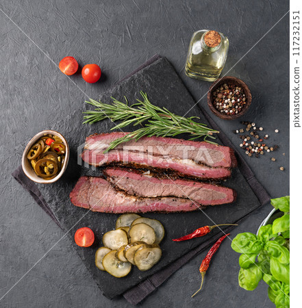 Grilled bbq brisket meat slices with jalapenos, herbs and pickled cucumber on a dark background.  117232151